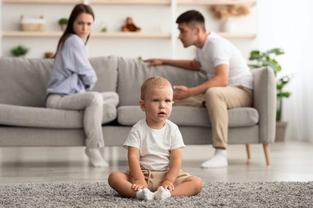 Domestic Quarrels. Cute infant baby boy sitting alone separately from arguing parents