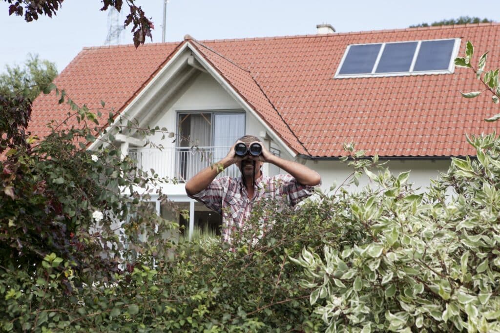 Man looking through binoculars over hedge